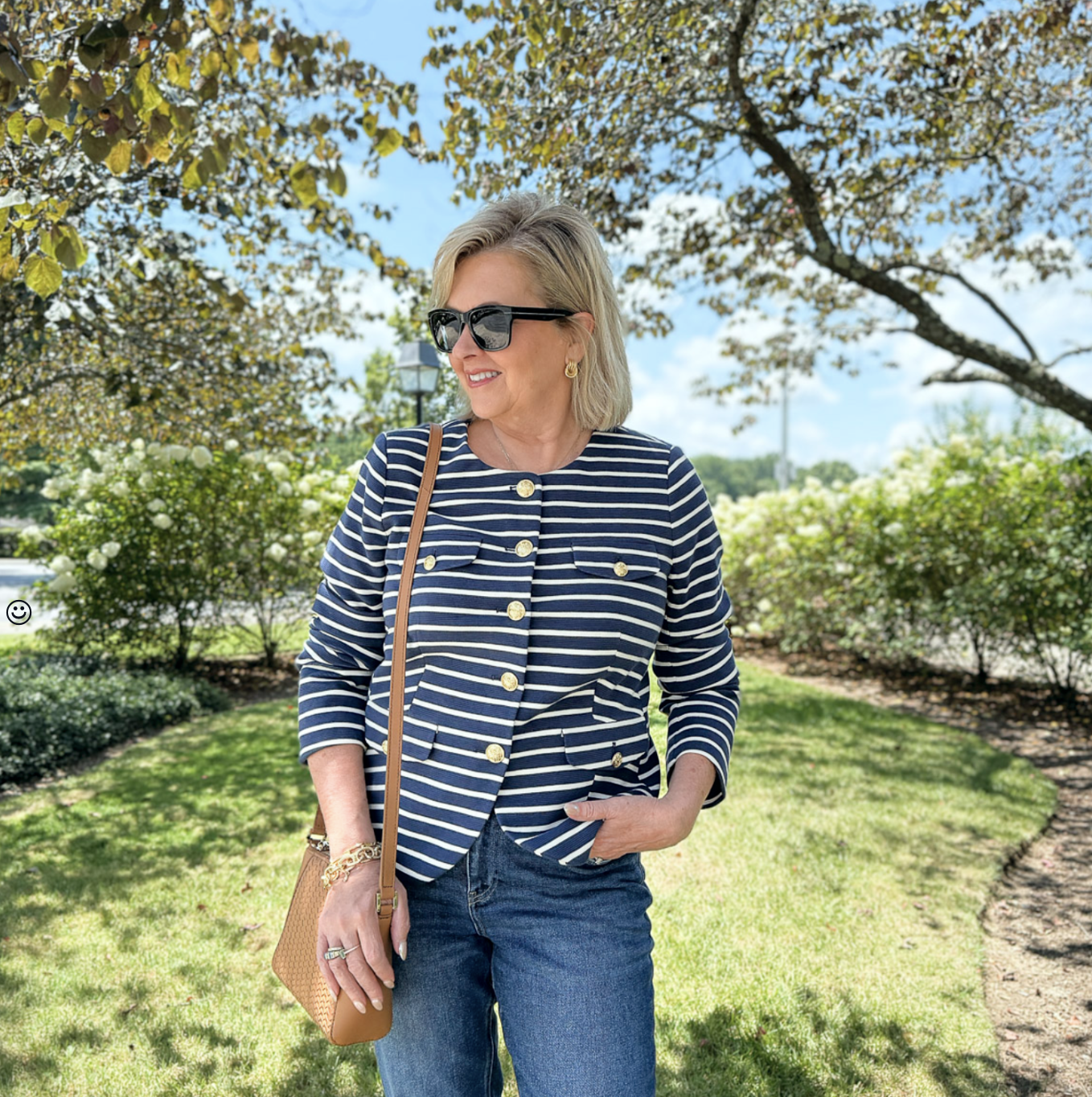 Woman over 50 in striped knit jacket and jeans with a neutral leather crossbody, styled for early fall
