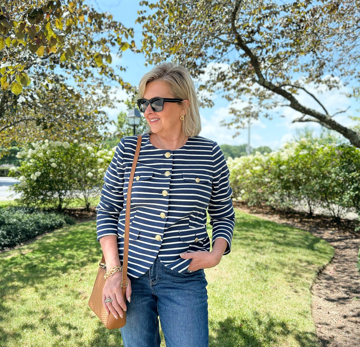 Woman over 50 in striped knit jacket and jeans with a neutral leather crossbody, styled for early fall