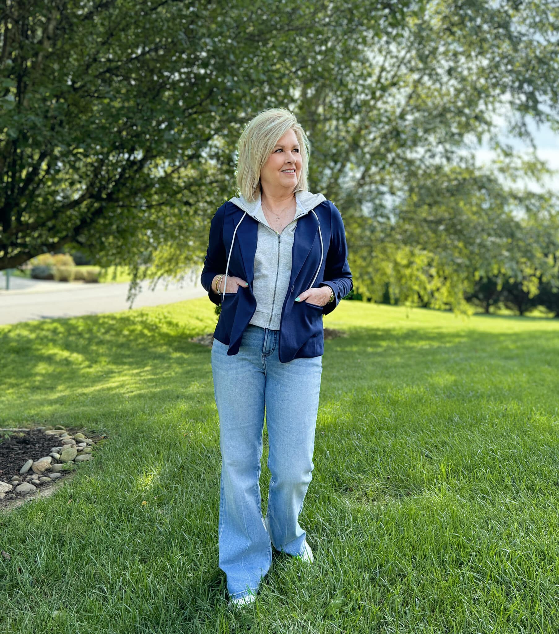 Woman over 50 standing in a grassy field in a navy and gray hoodie and light jeans from Kohl's