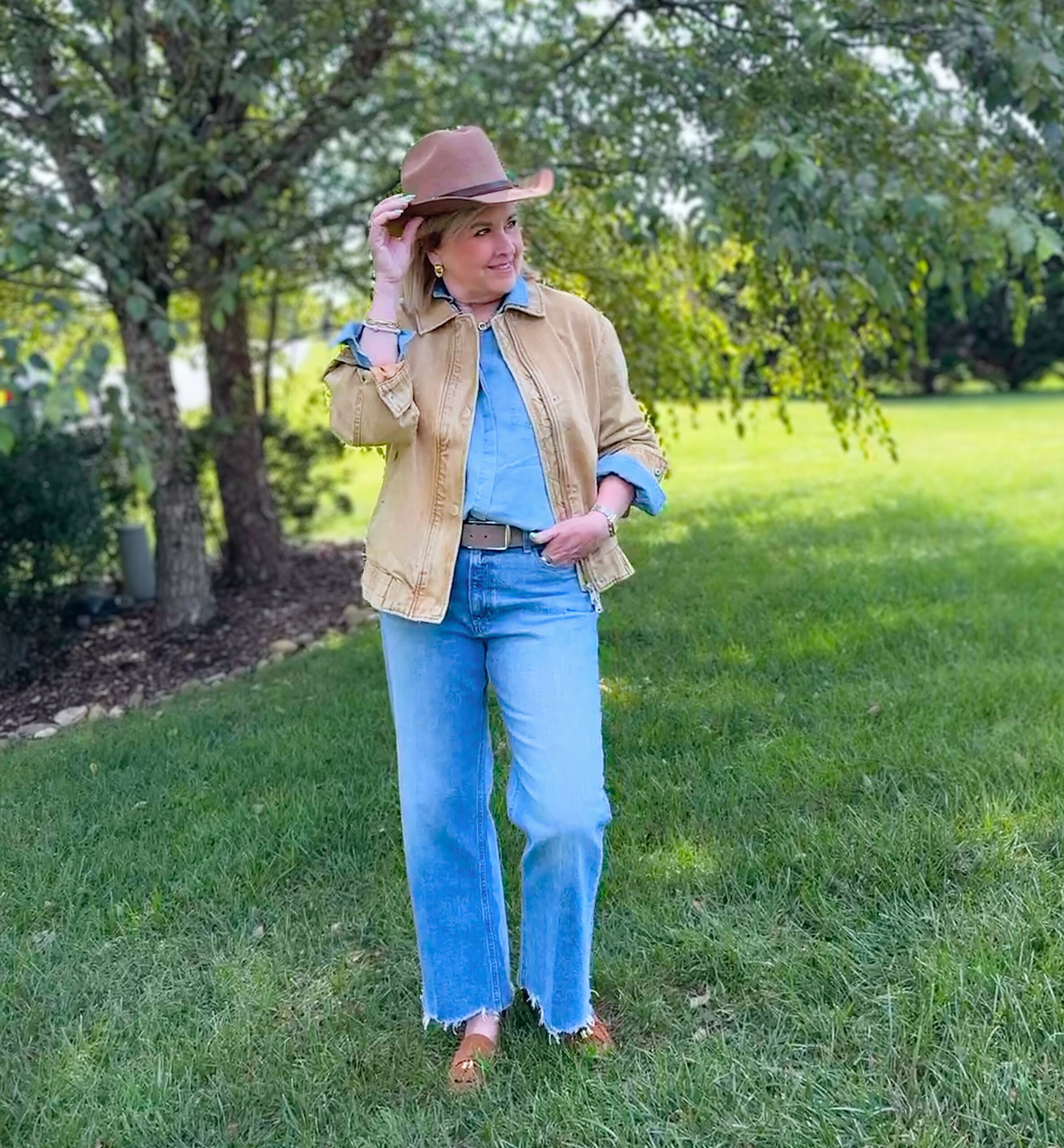 Western trend outfit for women over 50 featuring oversized denim jacket, chambray button-up, raw hem wide-leg jeans, and a cattleman’s crease cowboy hat.