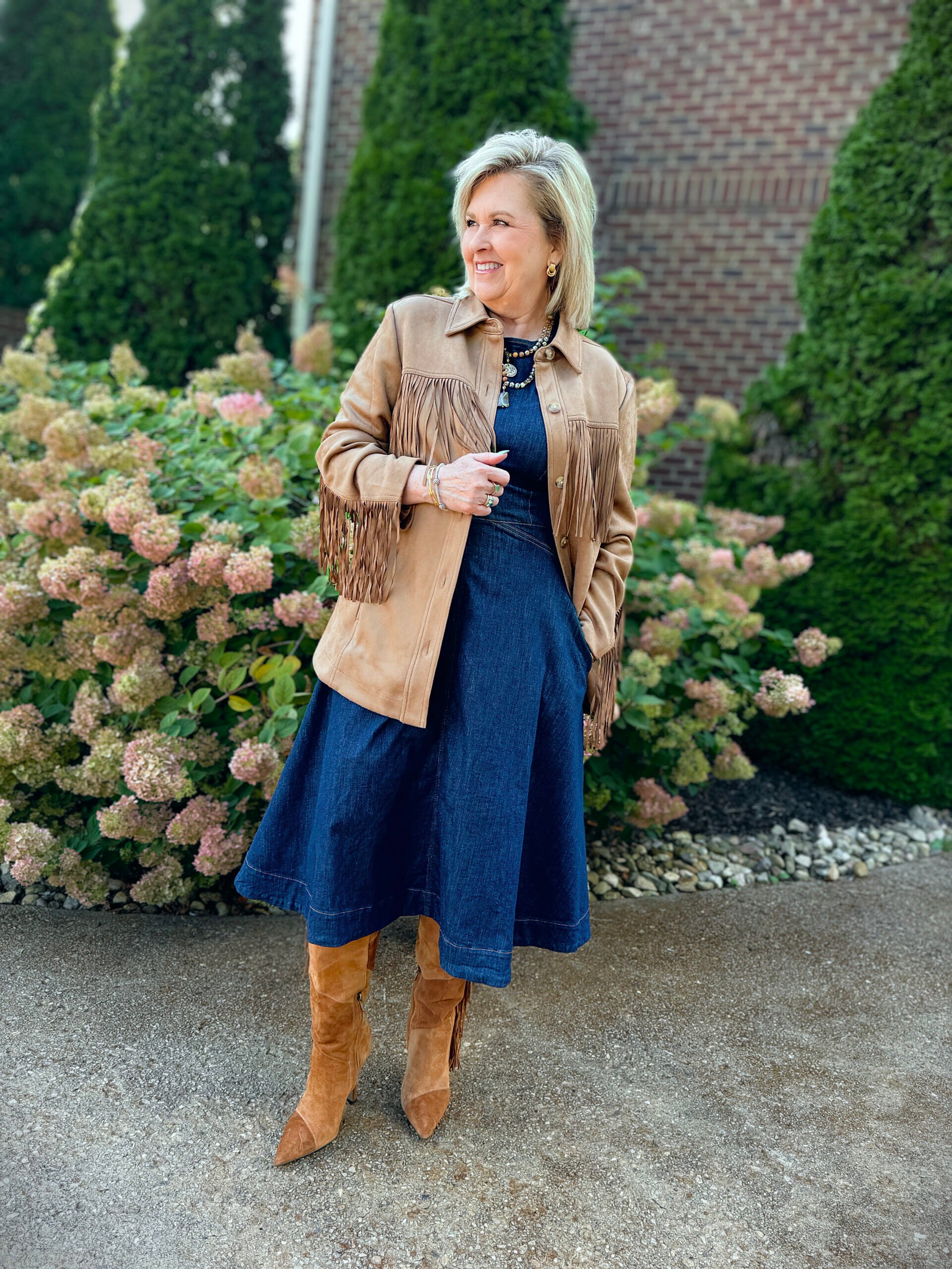 Tania Stephens wearing a fit and flare denim dress with a camel fringe jacket, a patchwork boots, and a crossbody handbag; both with fringe