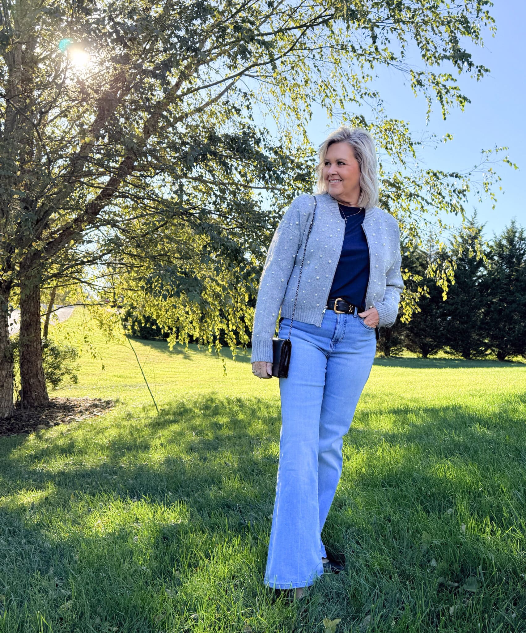 Tania Stephens standing under a tree wearing a Kohl's bomber jacket with pearls and lightwash jeans
