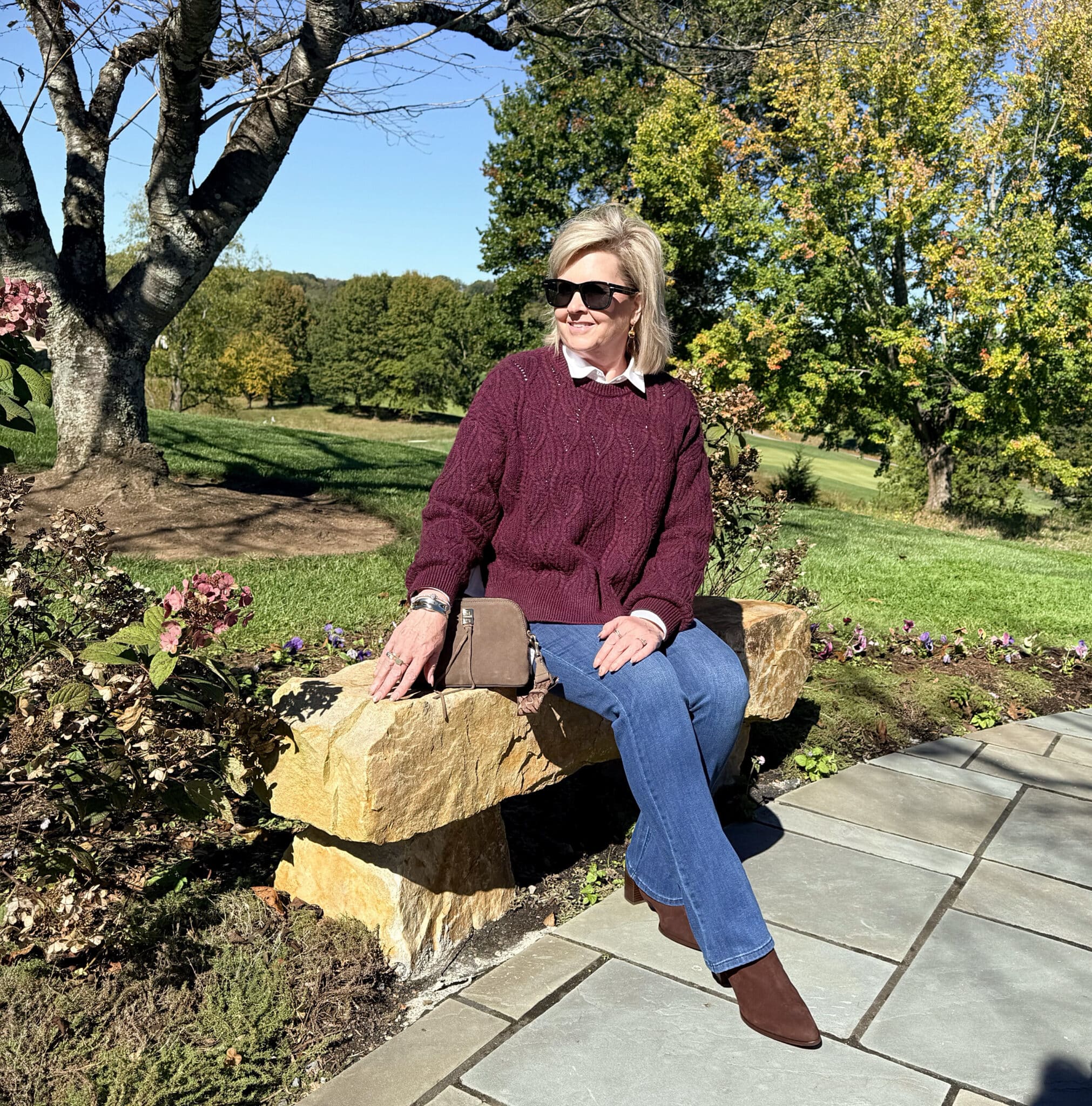 Nordstrom Rack sitting on a stone bench in a burgundy sweater with jeans and brown boots