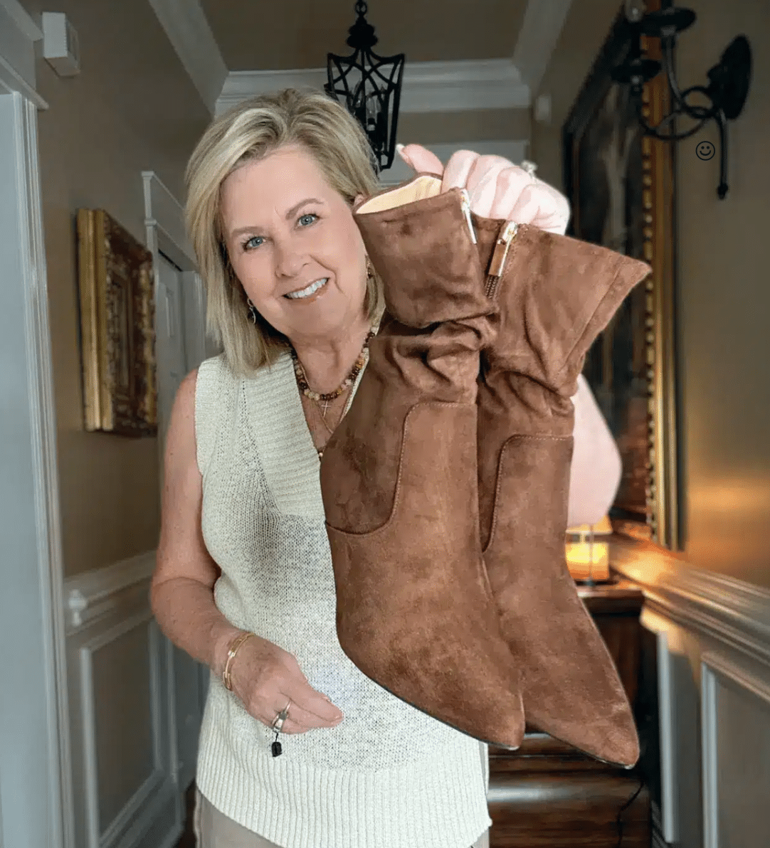 A WOMAN HOLDING UP A PAIR OF LEATHER OR SUEDE BOOTS FOR FALL WINTER 2025