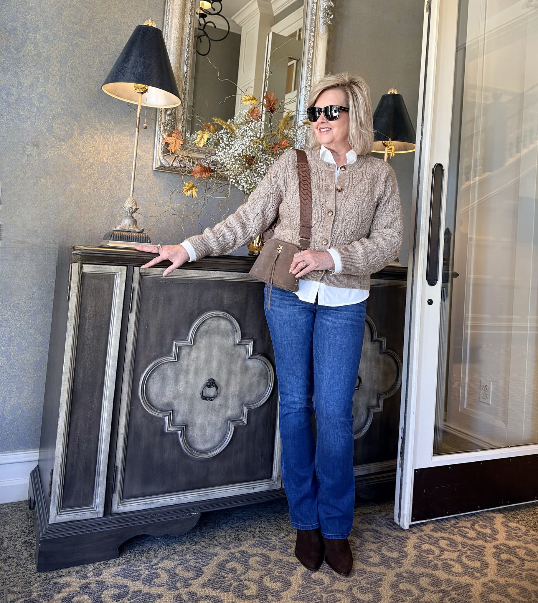 Tania standing by a table in a beige cardigan and jeans with brown boots