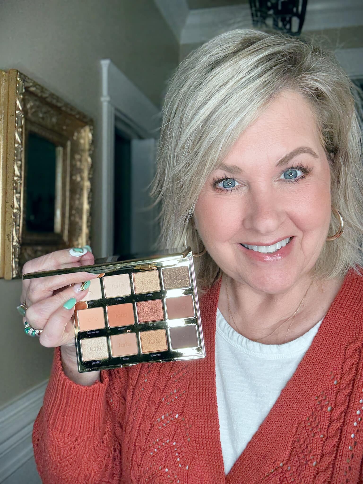 Tania in an orange sweater, holding a tarte Toasted Eyeshadow Palette