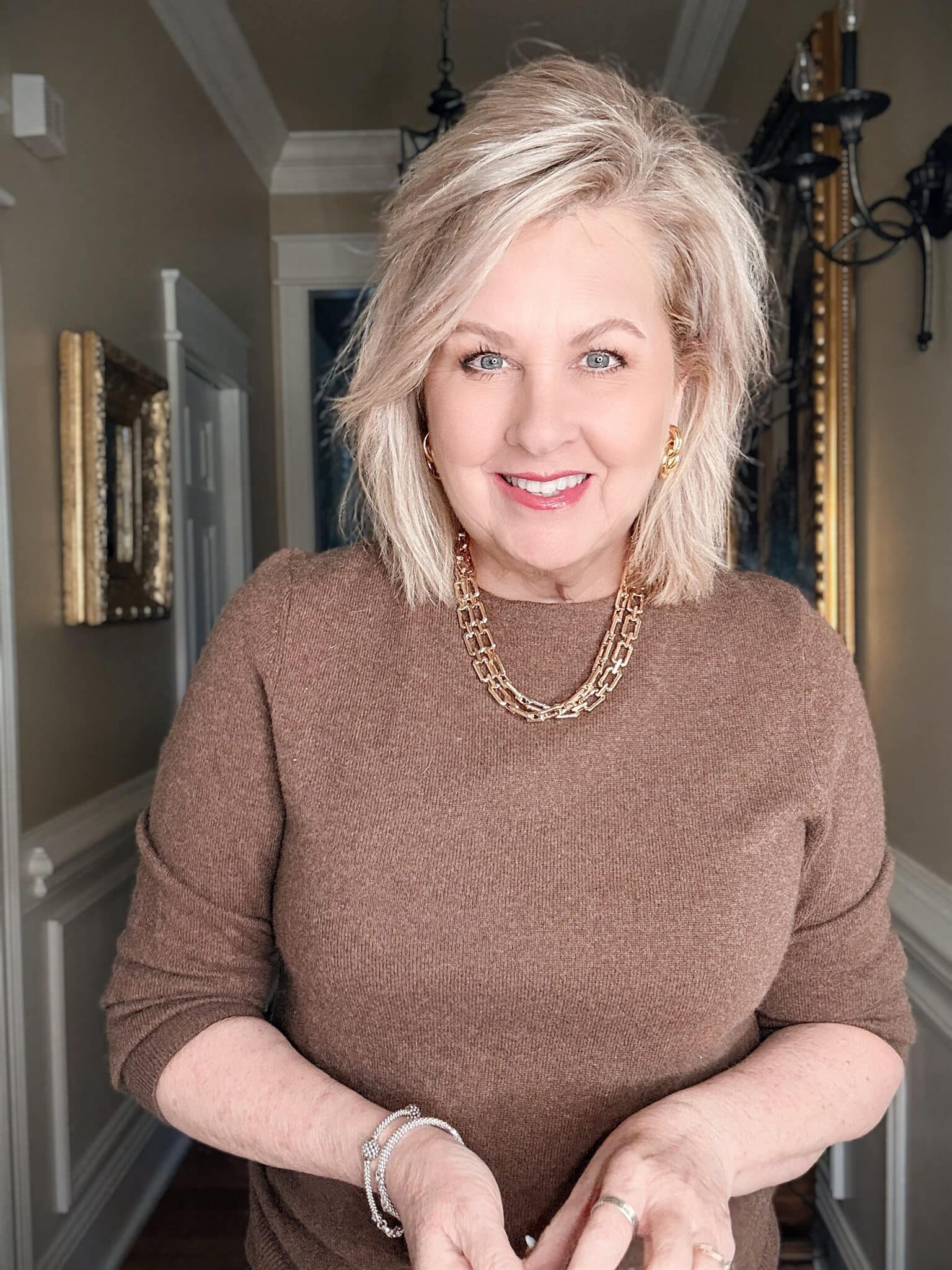 Woman wearing a thick gold chain necklace with a crew neck sweater, showing how statement necklaces elevate basic tops.