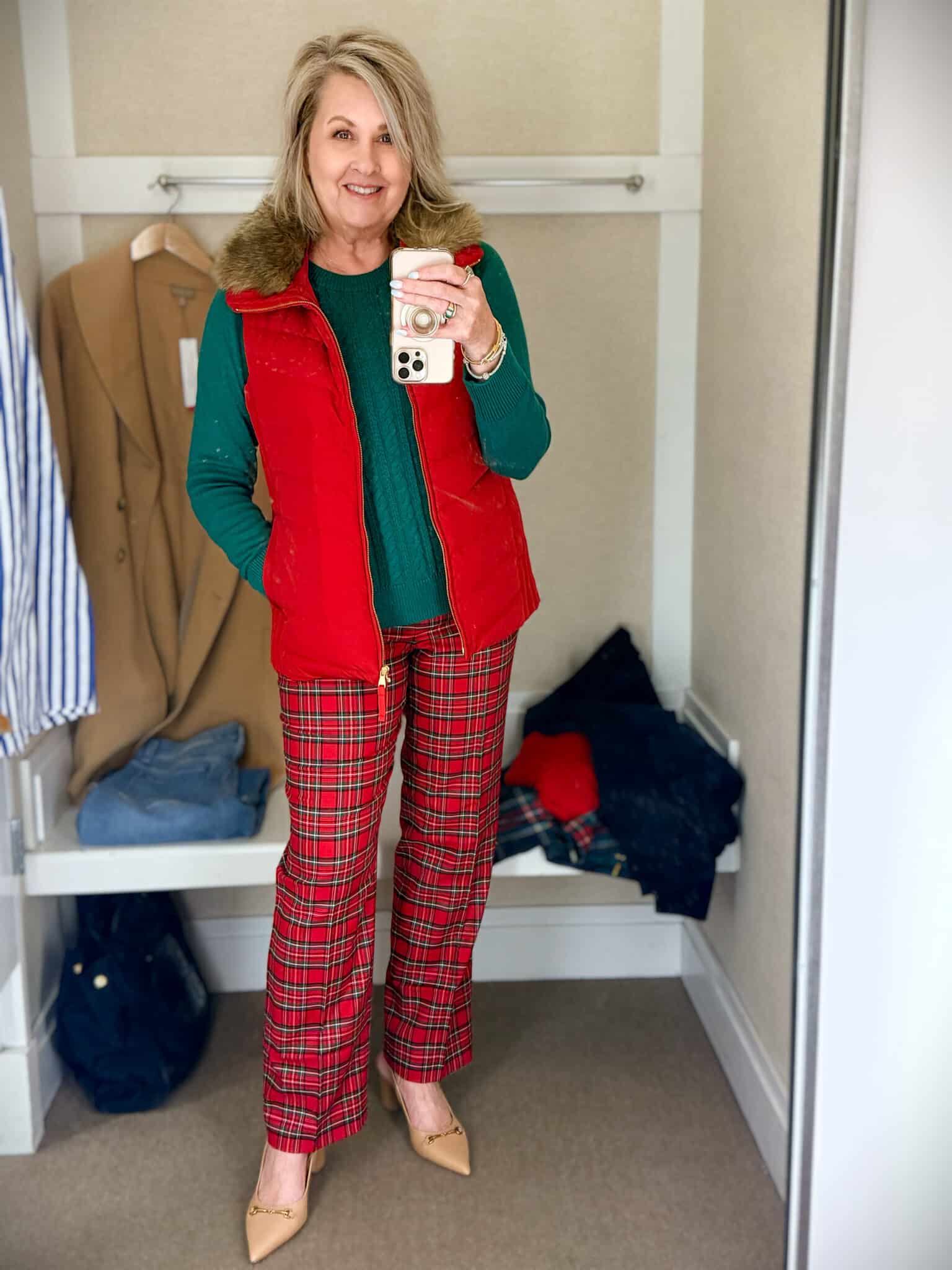 Tania trying on a green sweater with a red vest with a fur collar and red plaid pants from Talbots