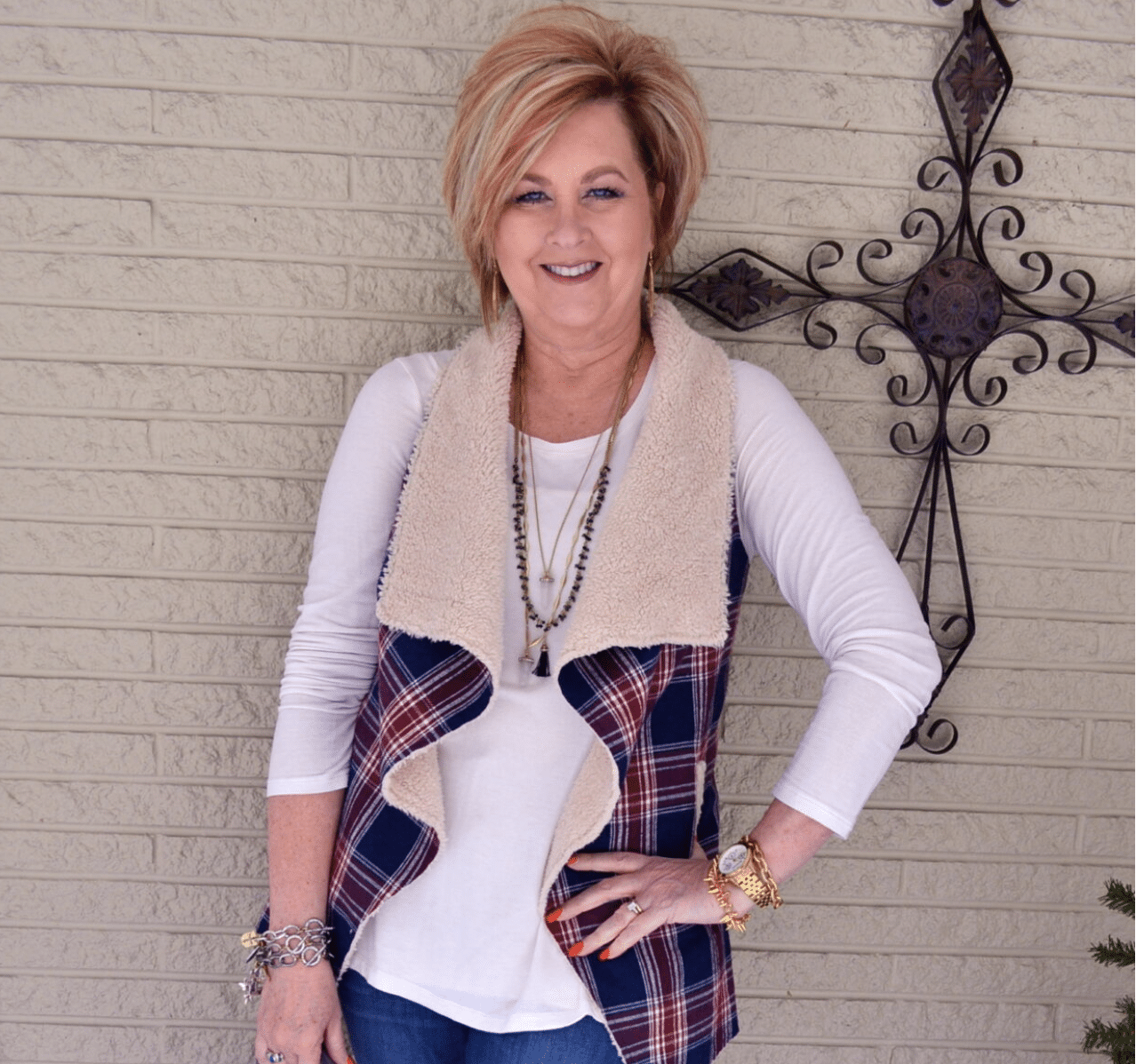 Tania wearing a plaid sherpa vest standing in front of a wrought iron cross in February 2016