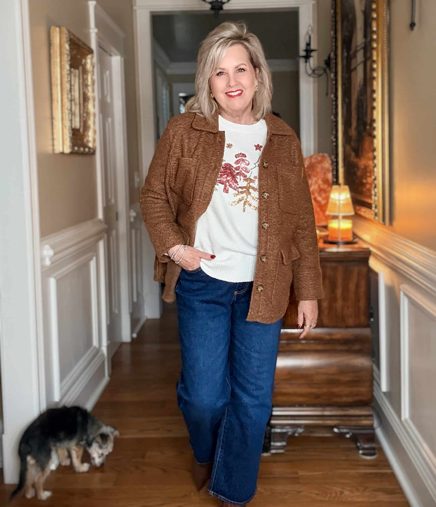 Tania wearing a white holiday sweater with a brown boucle coat and dark wash ankle jeans from Walmart