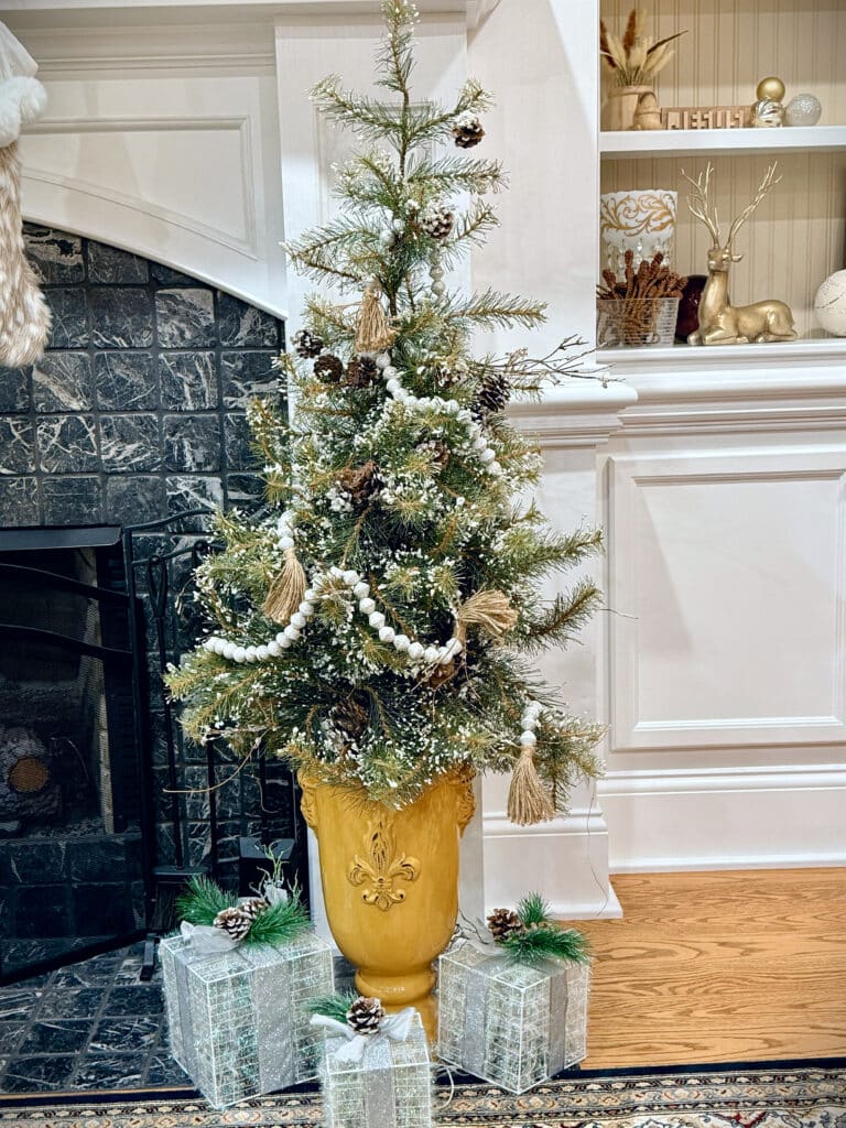 Small realistic Christmas tree in a yellow urn next to a fireplace
