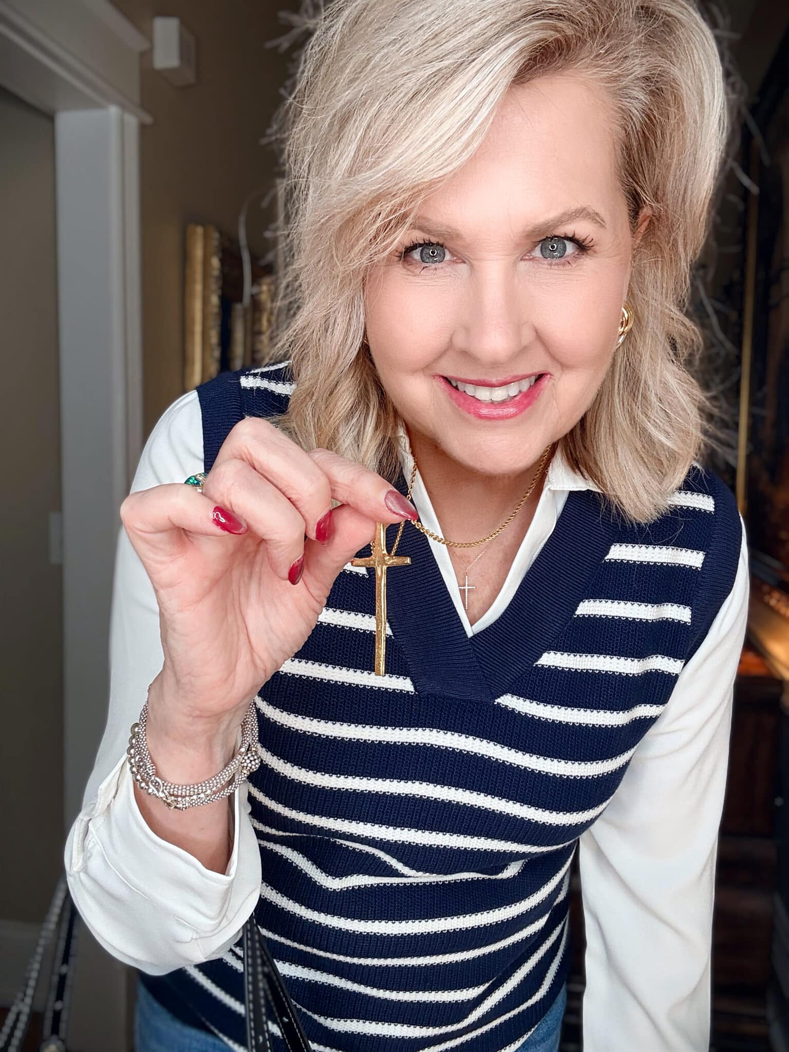 Tania wearing a sweater vest/white shirt combo with a gold hammered cross necklace