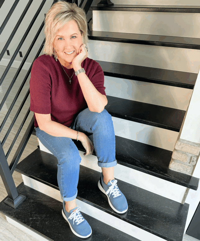 Tania sitting on the stairs wearing a sweater with jeans and slip on sneakers