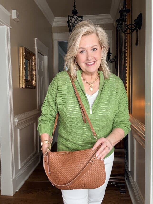 Tania holding a woven crossbody wearing a green sweater
