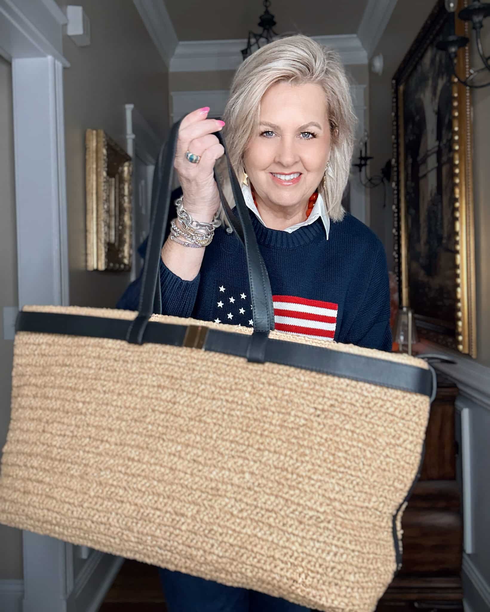 Tania wearing a white shirt with a navy American flag sweater with a large raffia handbag