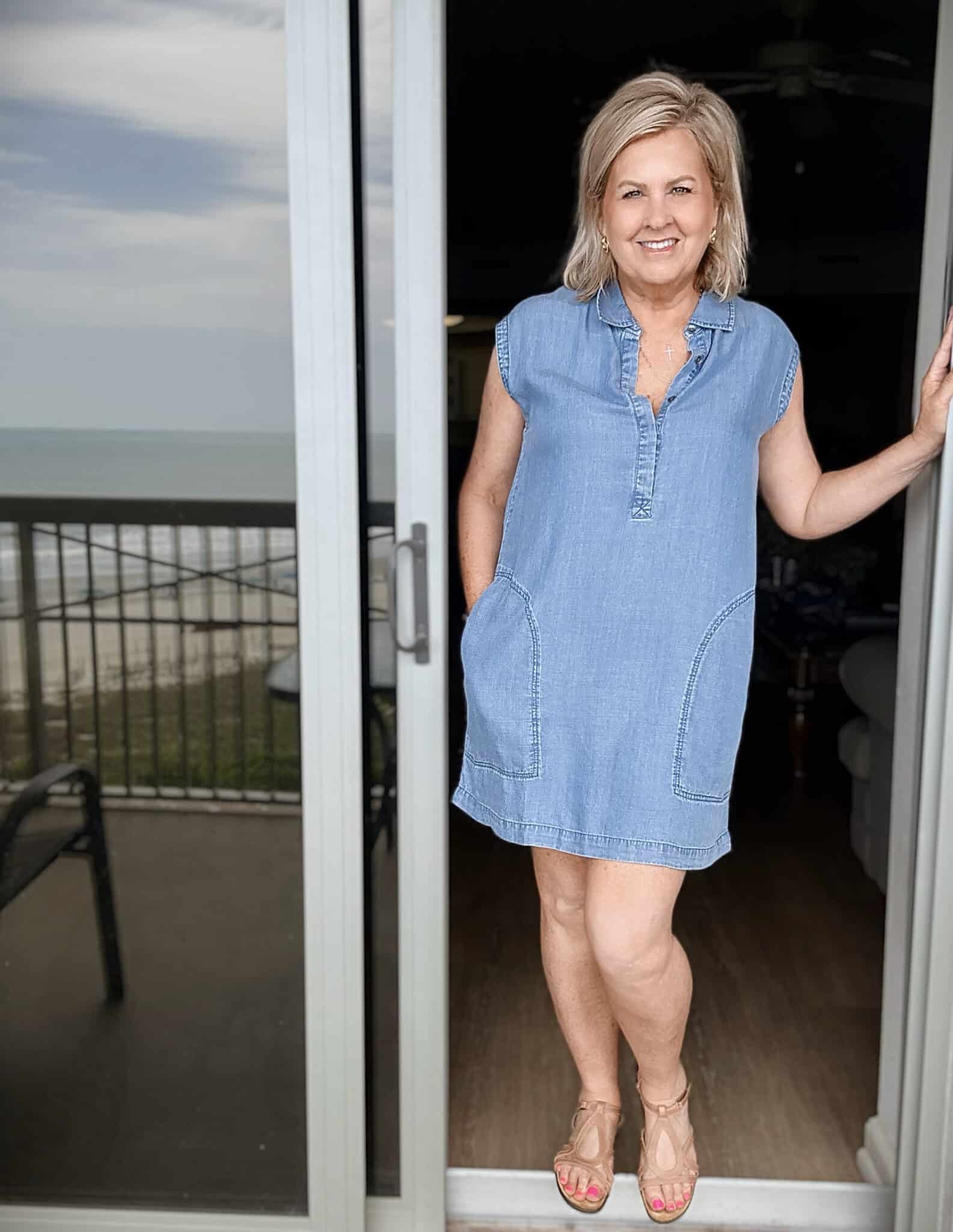 Woman over 50 wearing a chambray indigo mini dress with supportive tan cork sandals at the beach.