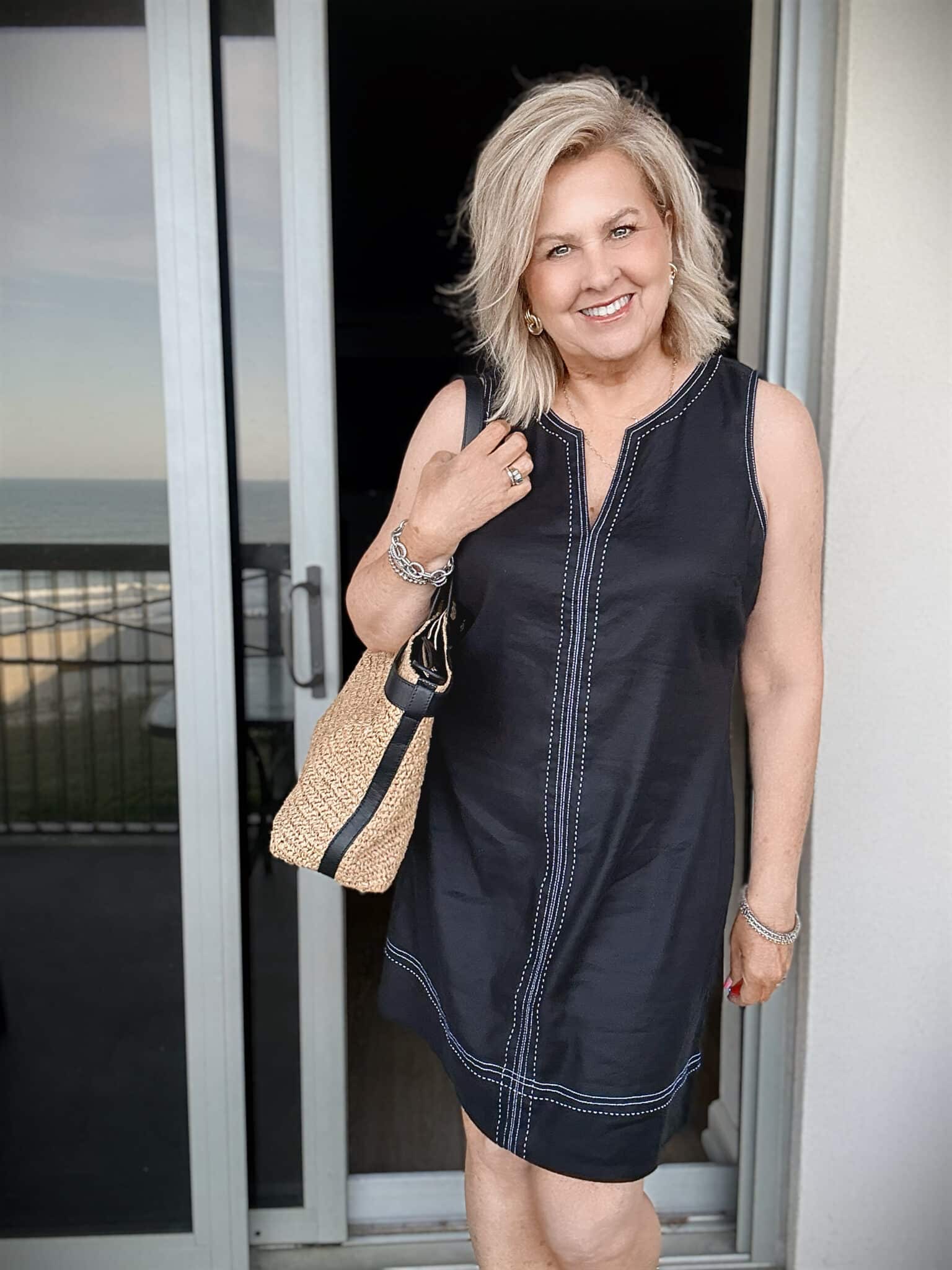Tania wearing a Tommy Bahama black sheath dress at the beach with a raffia bag