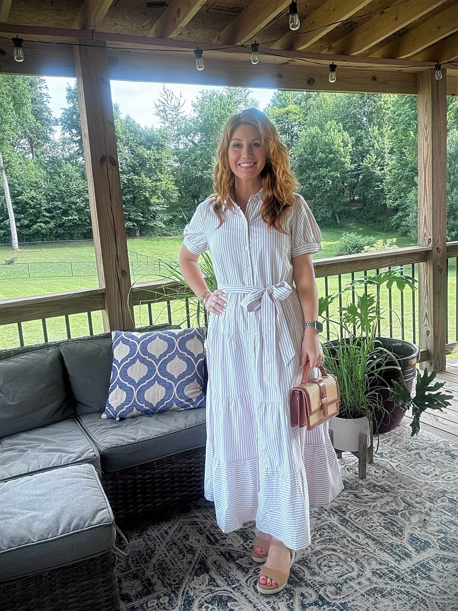 Petite woman wearing a striped maxi shirt dress with espadrille sandals and straw handbag