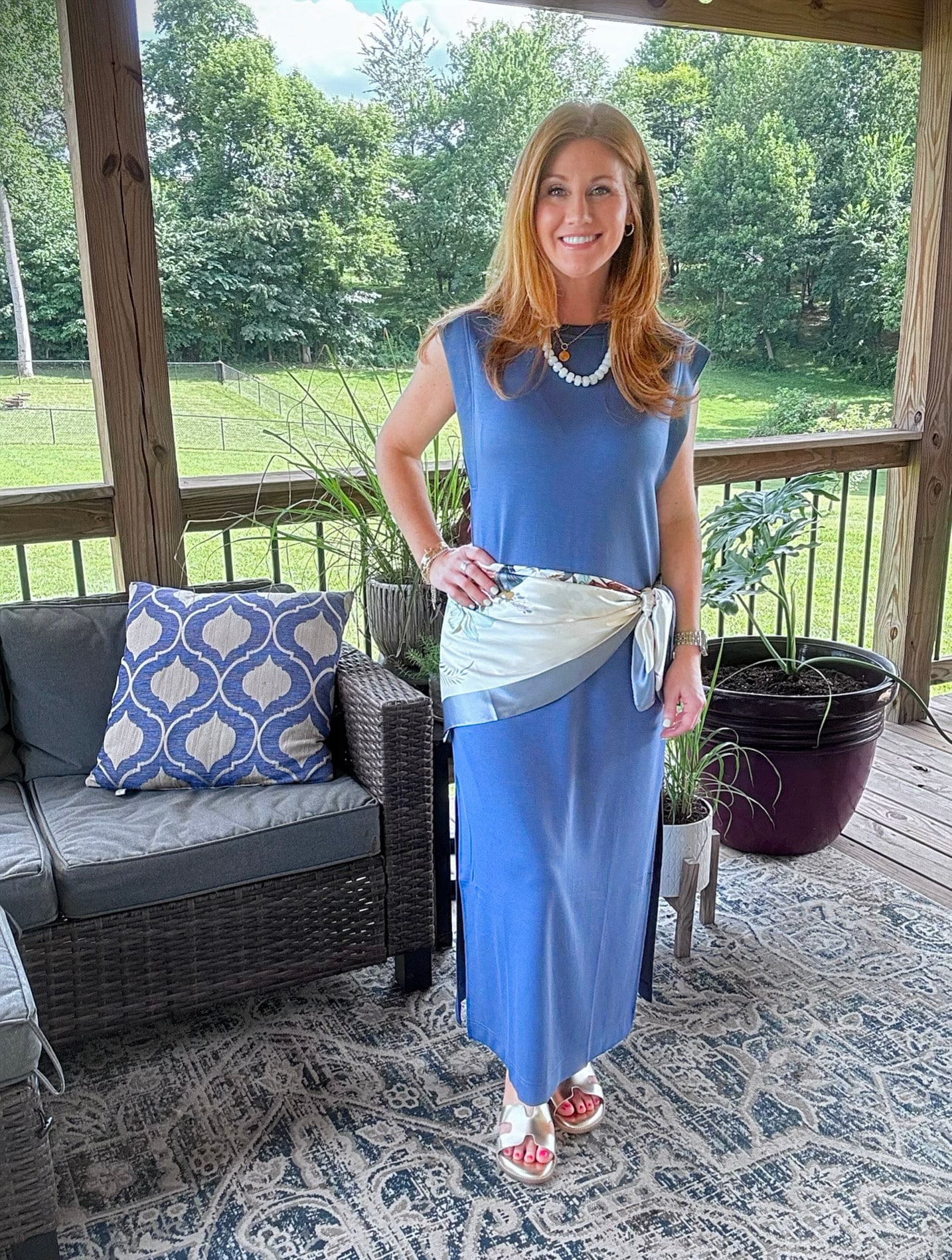 Petite woman wearing a blue sleeveless maxi dress styled with a satin scarf and beaded necklace