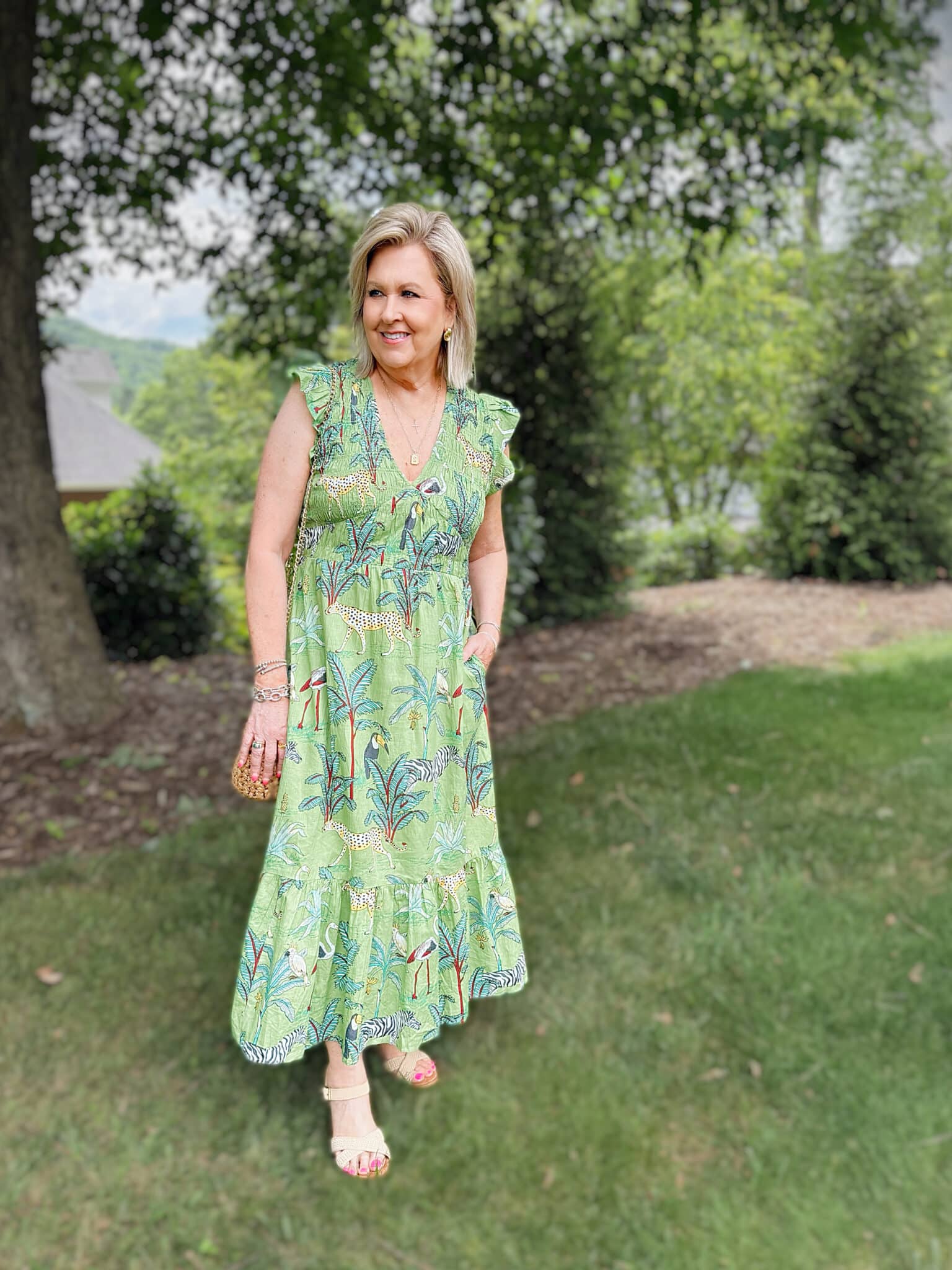 Woman over 50 wearing a green animal print tiered maxi dress with neutral sandals for a summer party or vacation dinner.