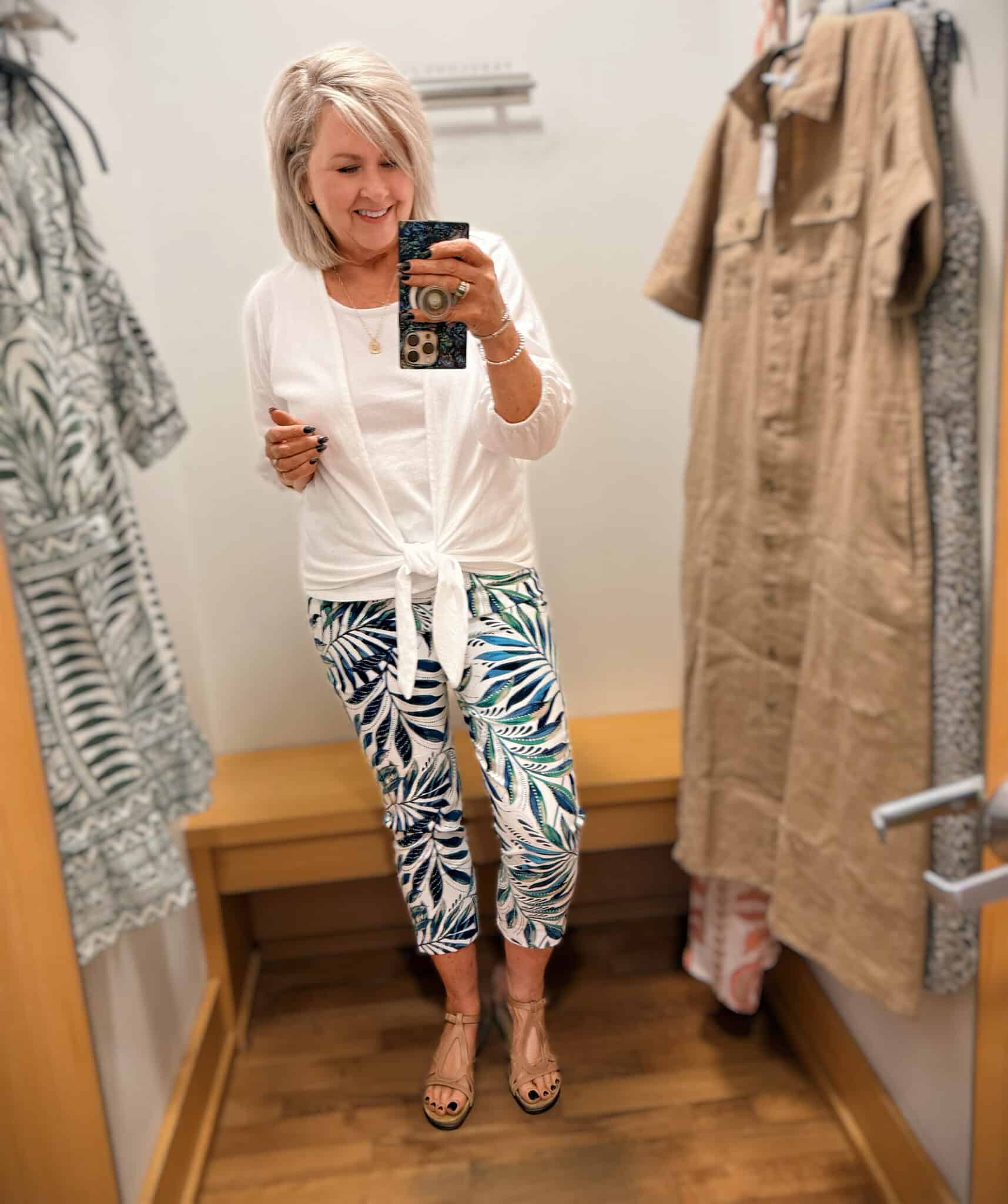 Tania Wearing a white tie cardigan and white tank top with a palm print pair of pants.