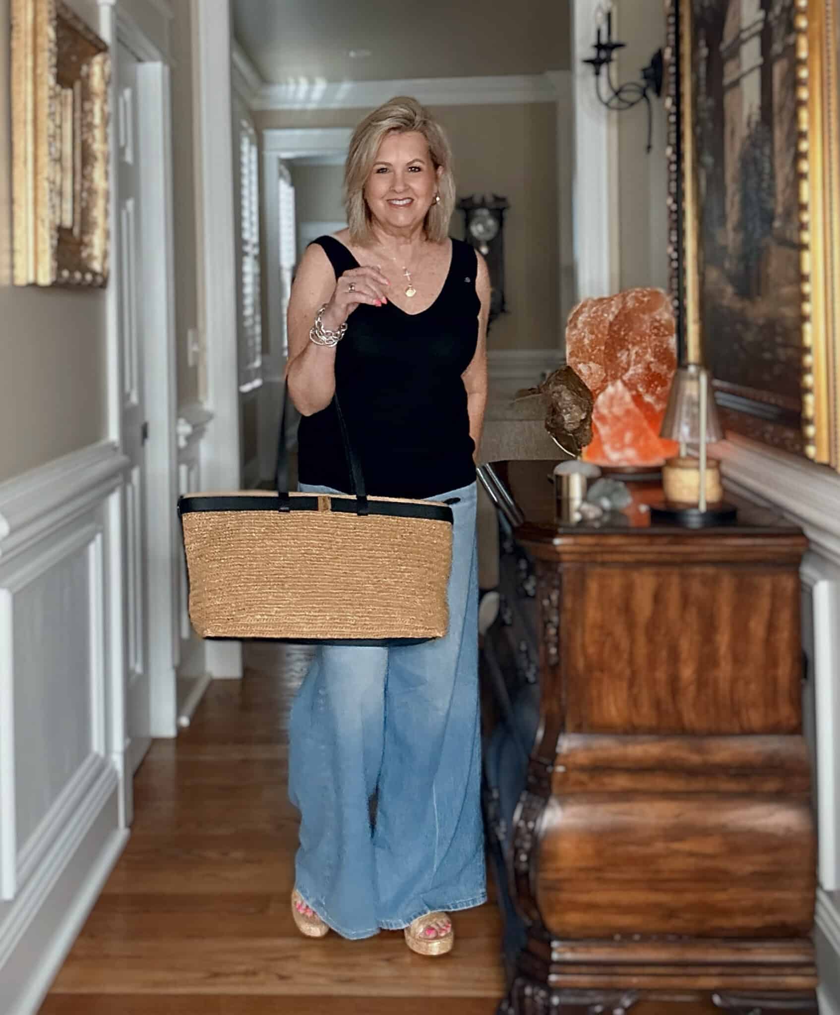 Woman over 50 wearing a black sleeveless sweater with light-wash wide-leg jeans