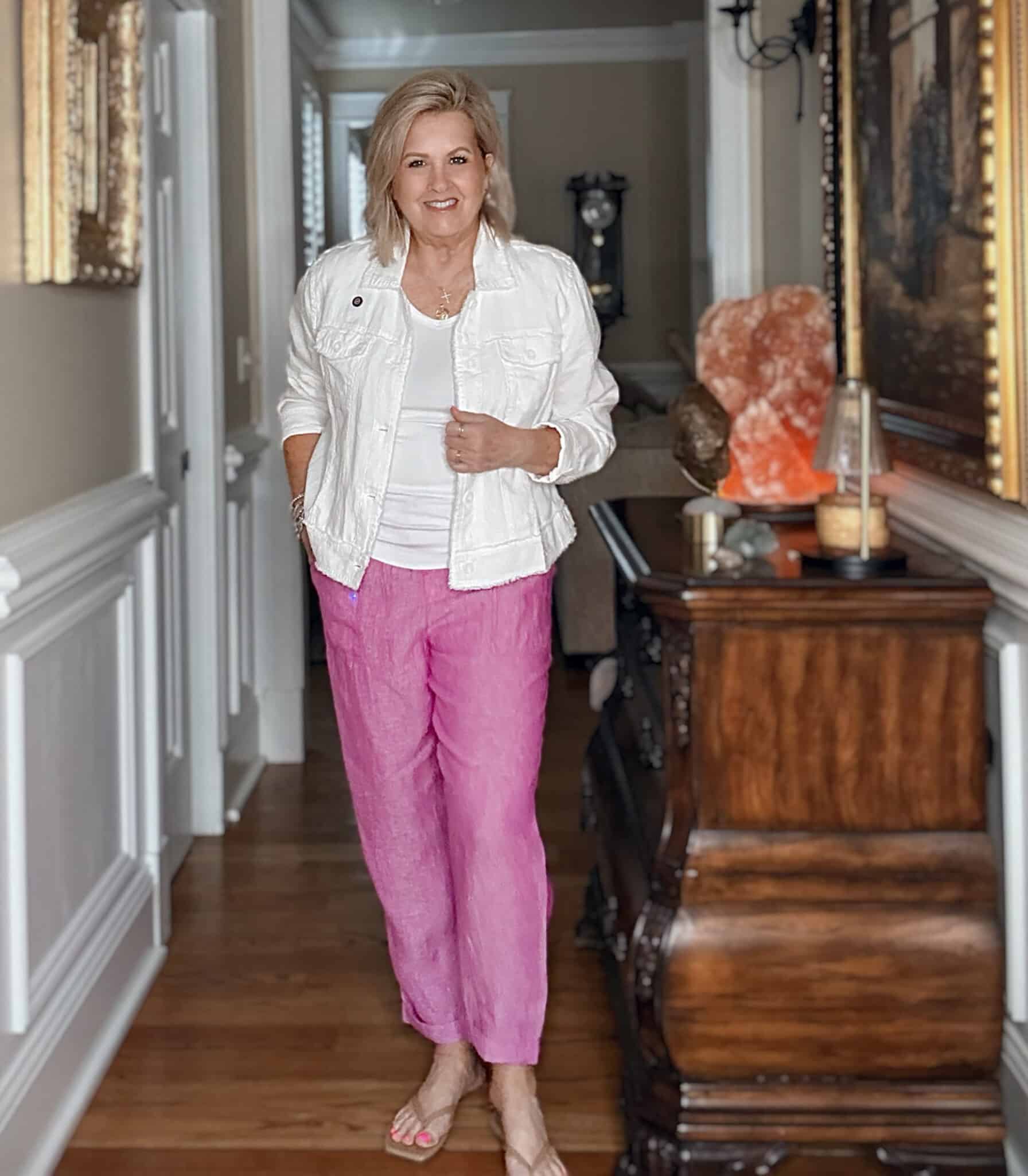 Woman over 50 wearing a white linen jacket with pink linen pants and neutral sandals
