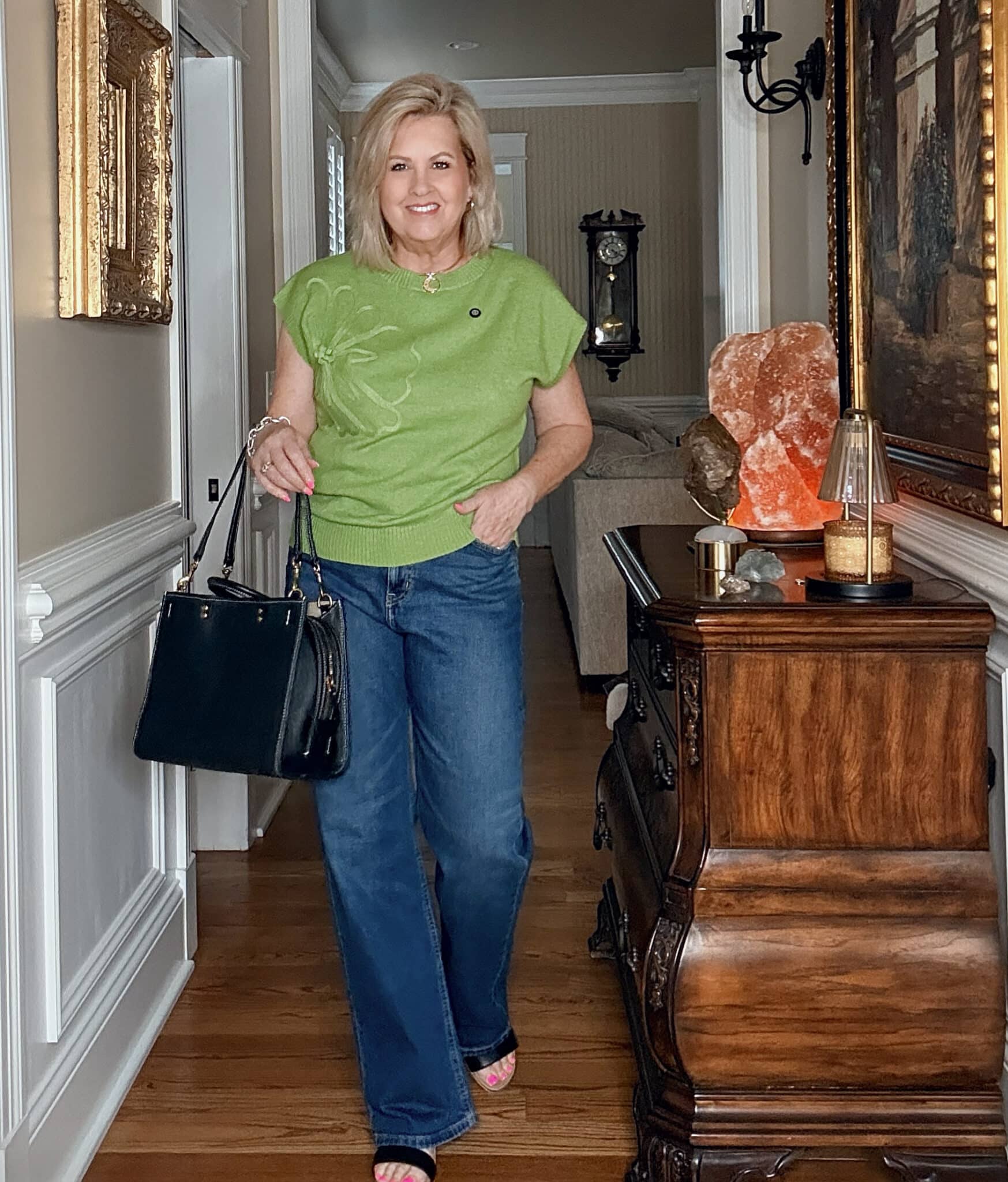 Woman over 50 wearing a green floral embellished sweater with dark wide-leg jeans