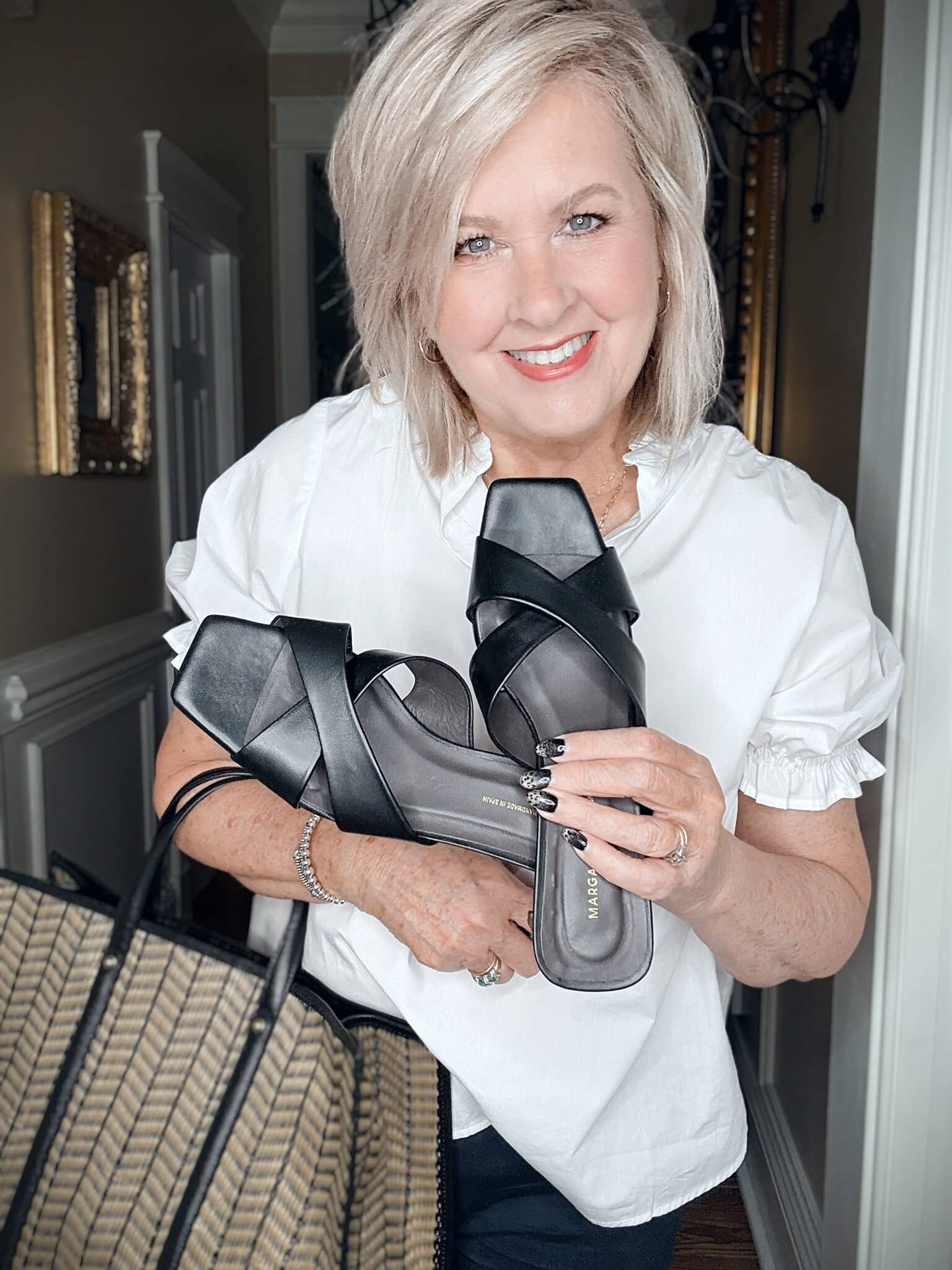 Tania wearing a white puff sleeve top holding Margaux black sandals