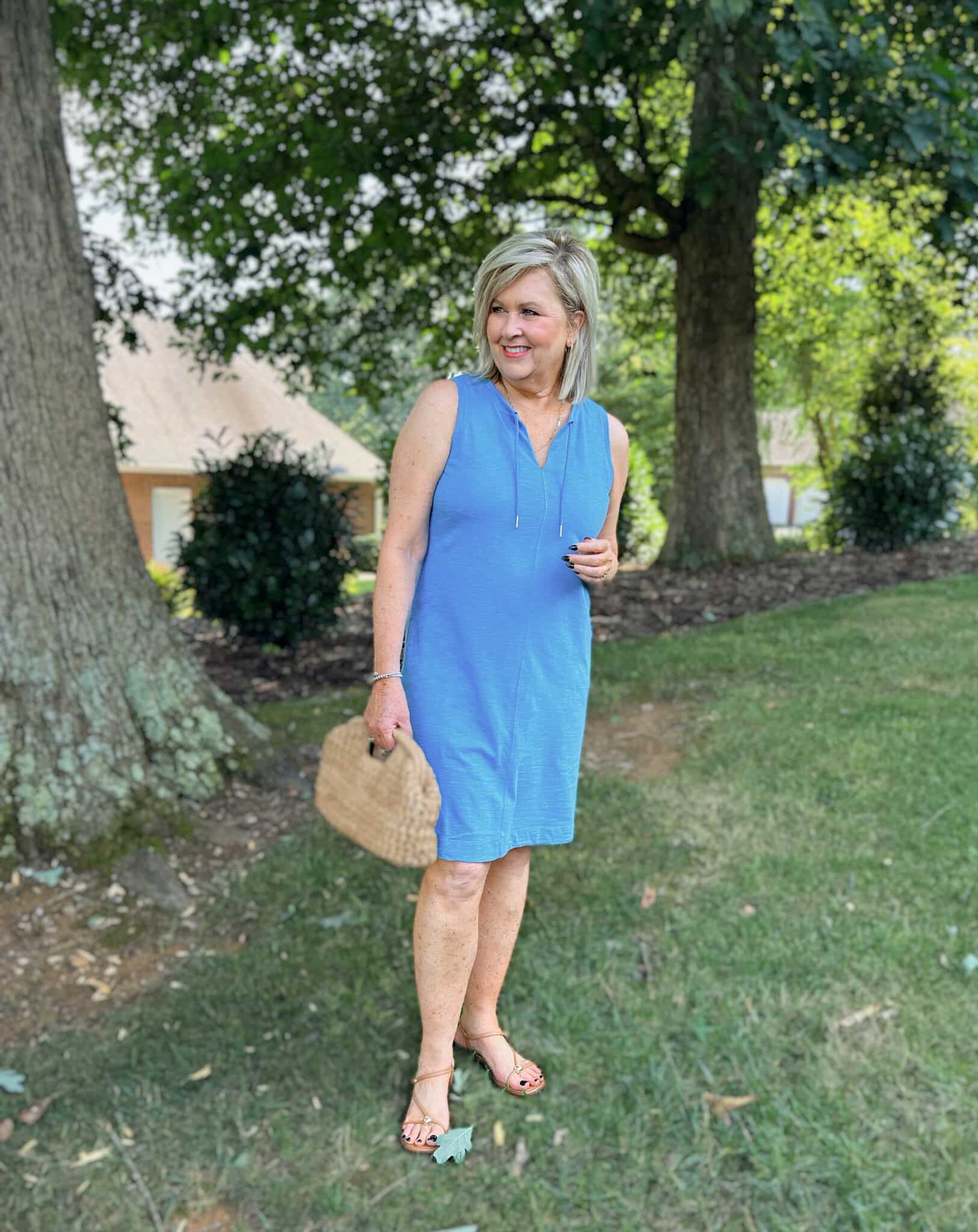 Tania wearing a solid blue tank dress with raffia clutch and flat sandals