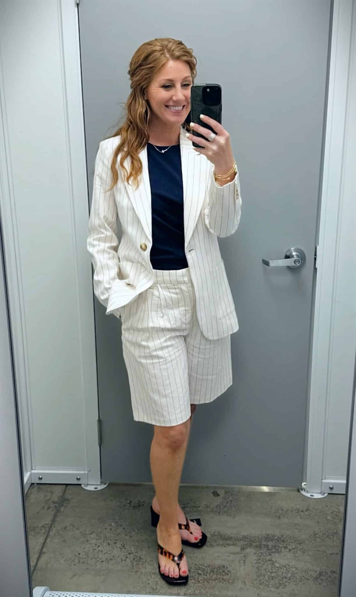Stephanie wearing an ivory pinstriped linen-blend blazer and matching pleated Bermuda shorts with a navy top and lucite sandals.