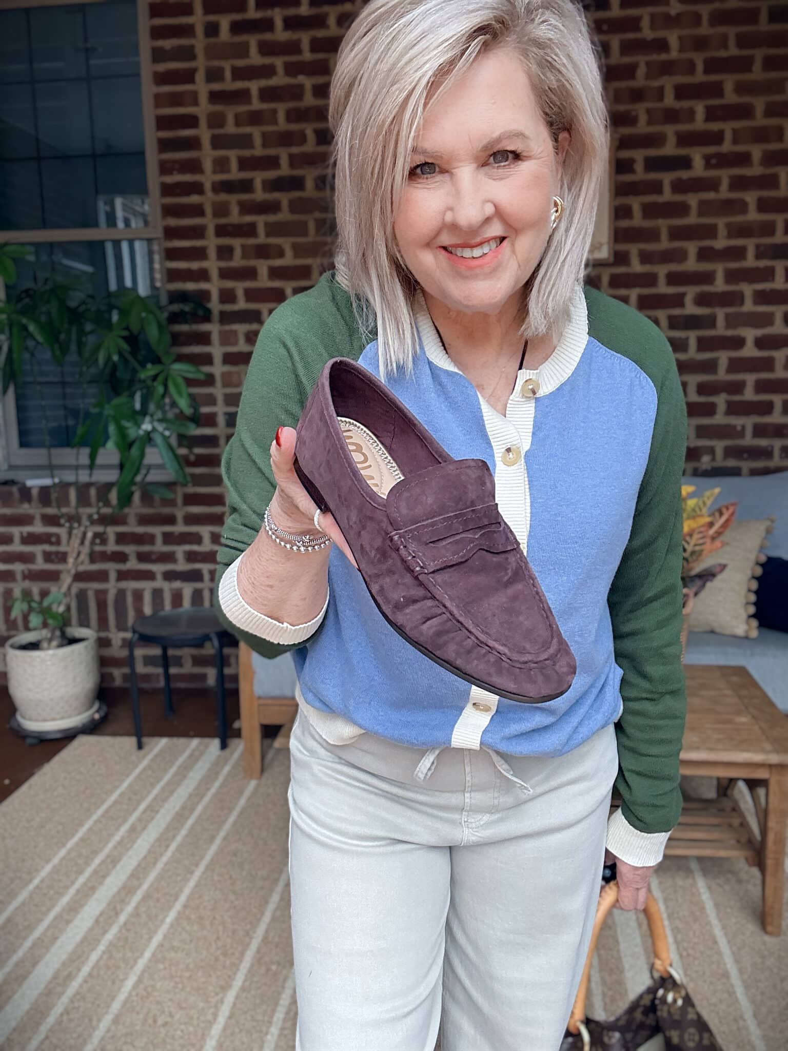 Tania wearing a colorblock sweater holding a brown loafer for fall