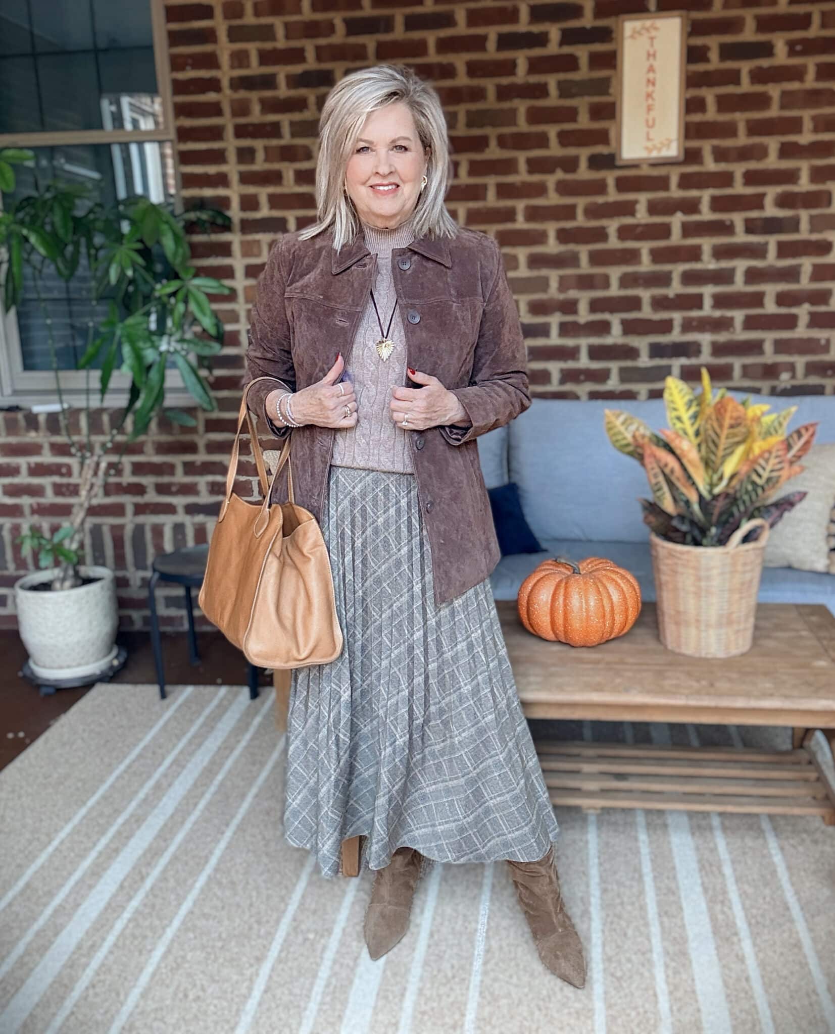 Tania wearing a chocolate brown suede jacket with a light brown sweater vest, a pleated olive skirt, and brown boots for fall