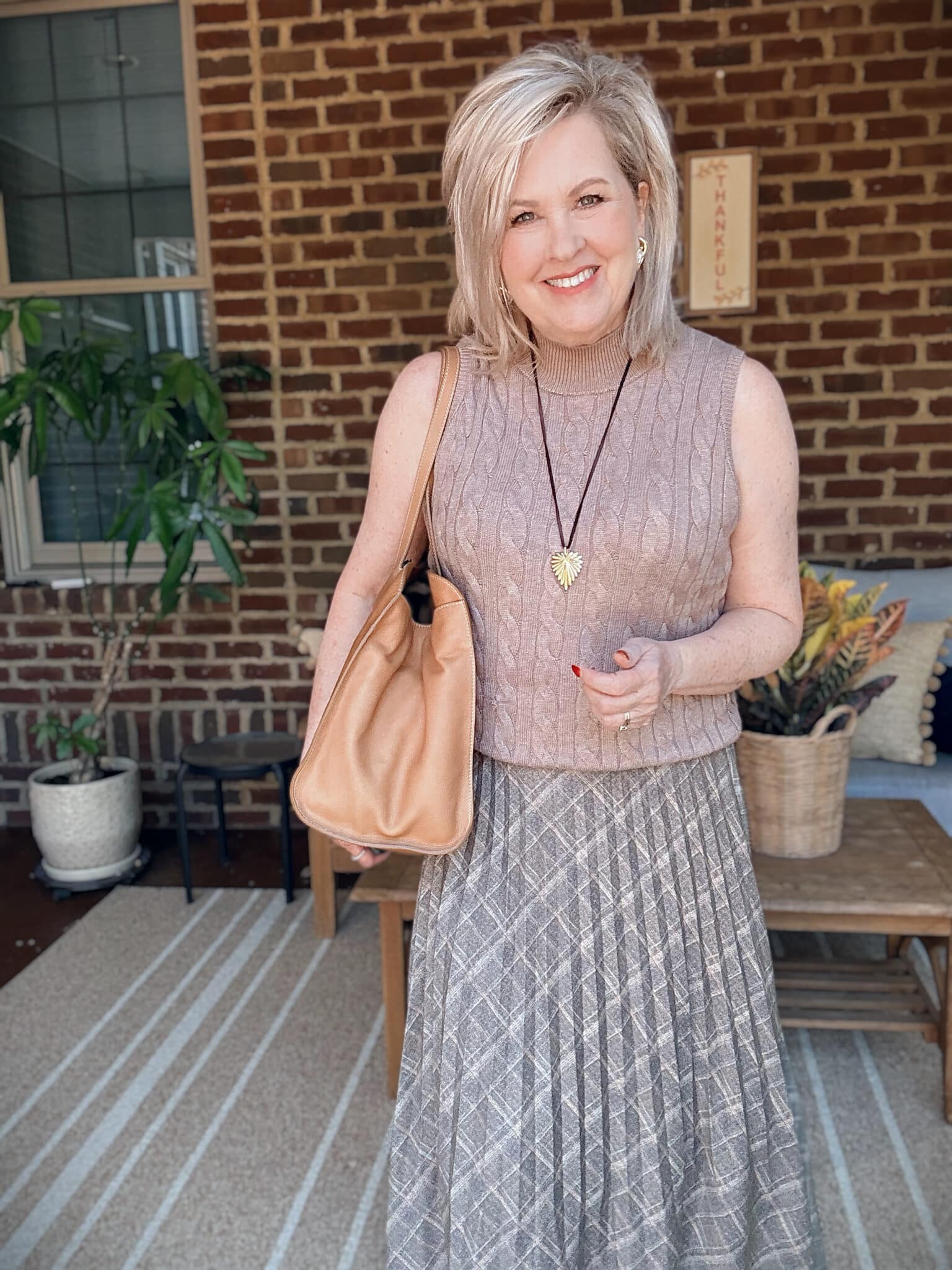 Tania wearing a light brown sweater vest with a pleated olive skirt