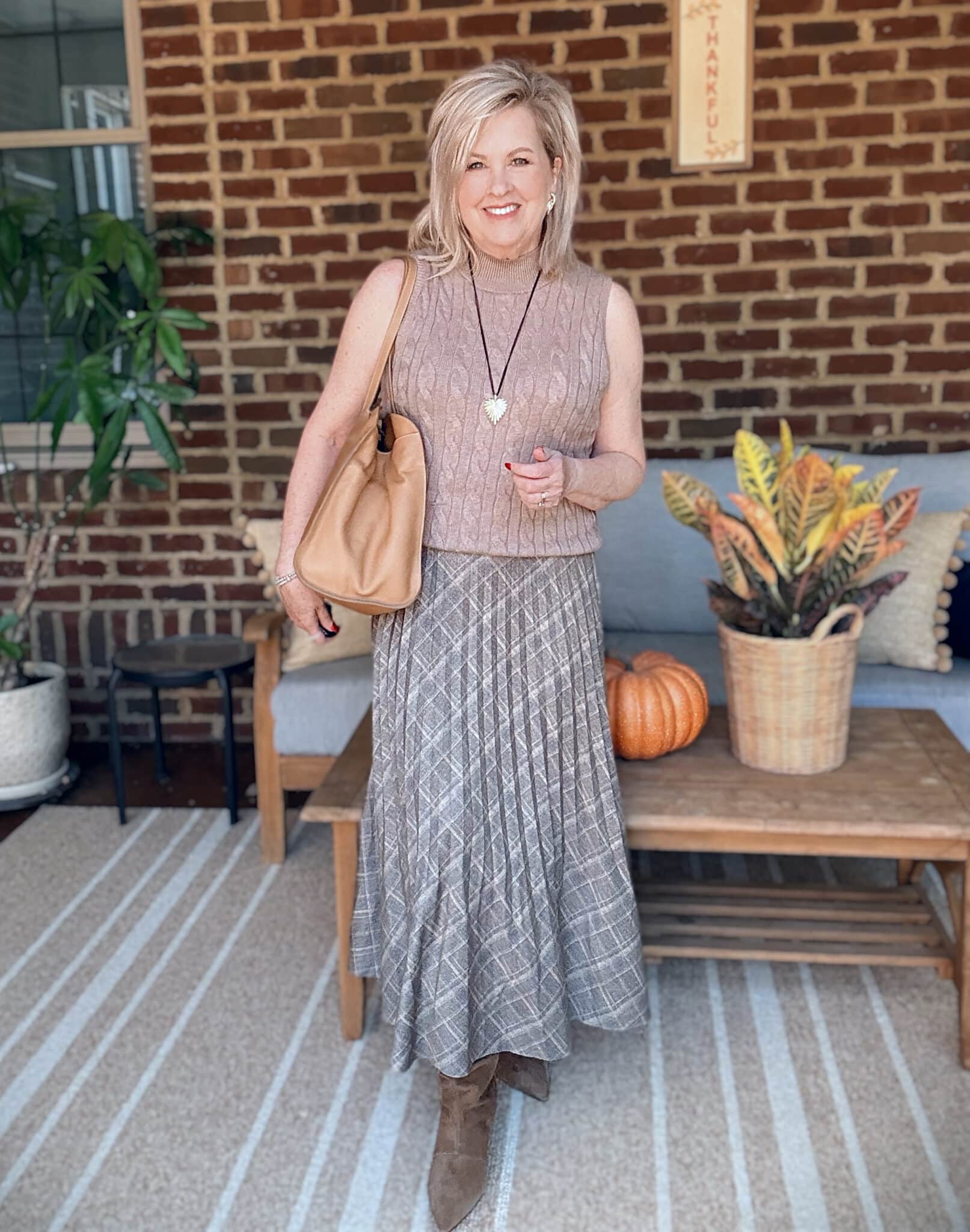 Tania wearing a light brown sweater vest with a pleated olive skirt and brown boots for fall