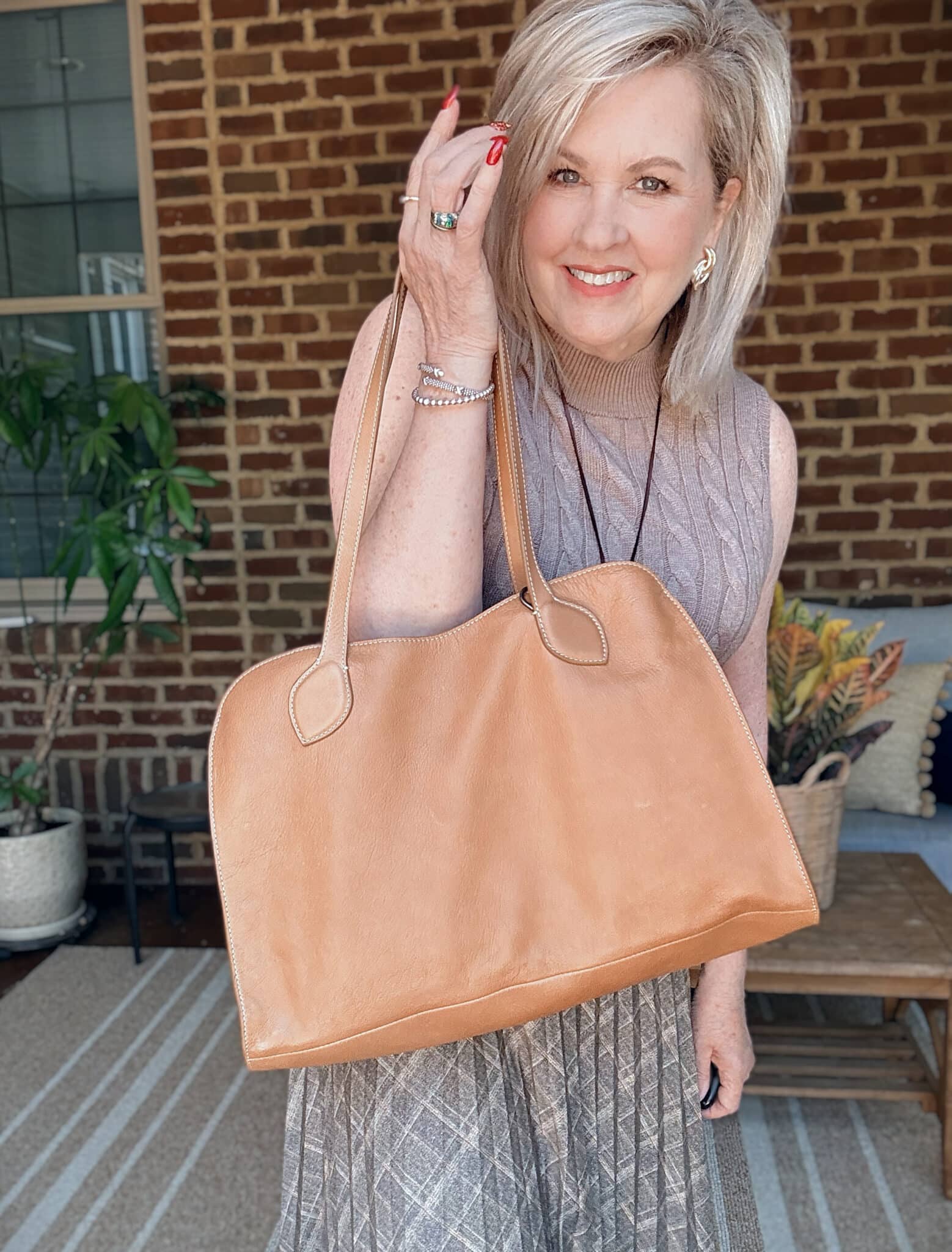 Tania wearing a light brown sweater vest holding a caramel leather tote