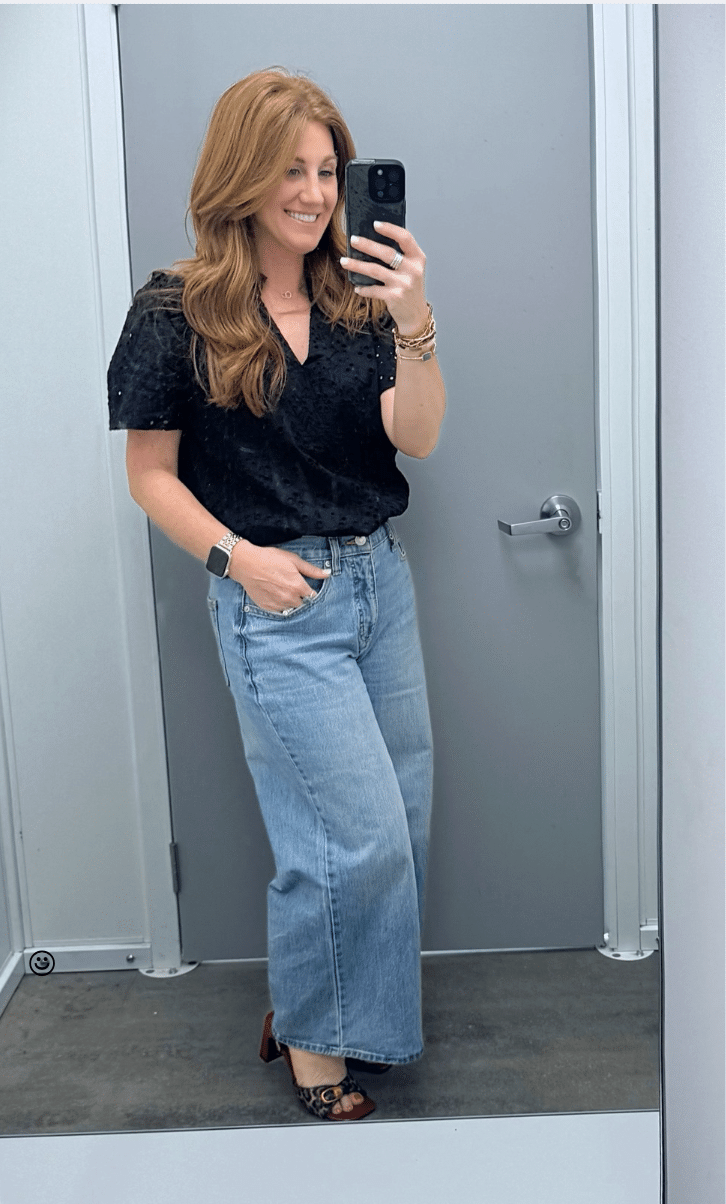 Petite woman showing a black eyelet top with wide leg jeans