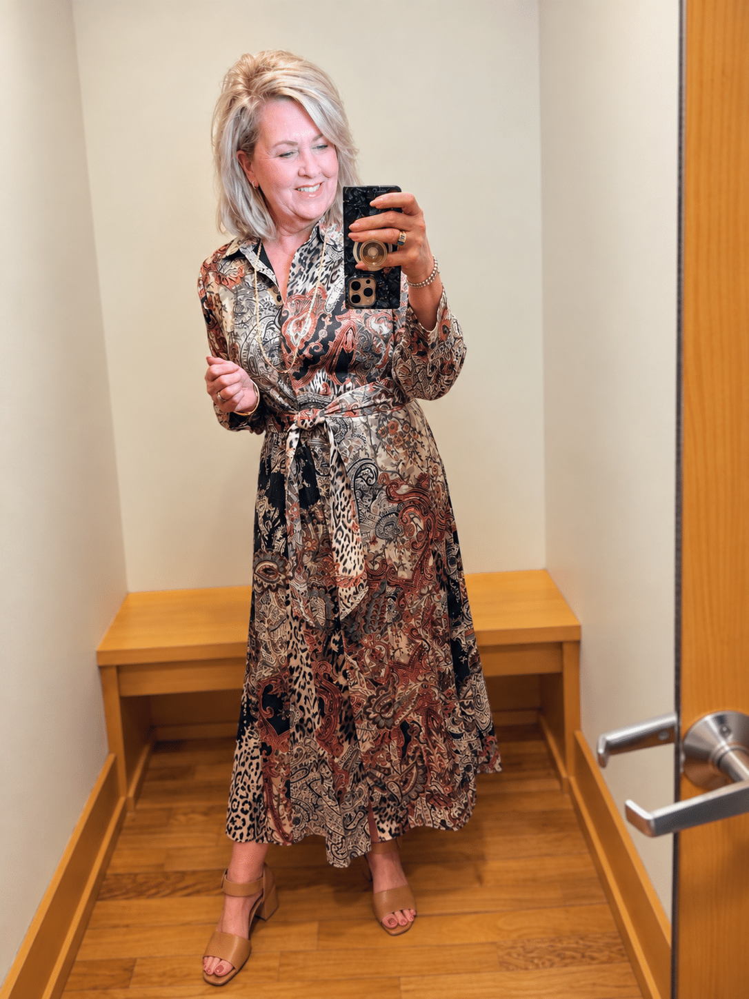 Woman over 50 wearing a Chico’s belted printed chiffon shirtdress with tan block-heel sandals.