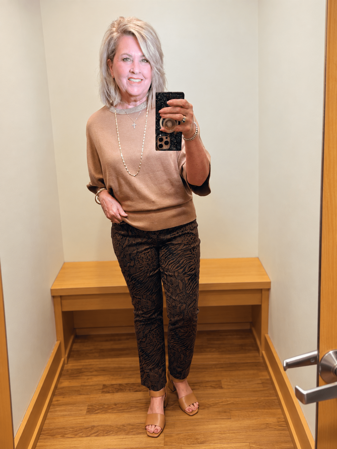 Woman over 50 wearing a Chico’s camel sweater with brown animal print slim ankle jeans.