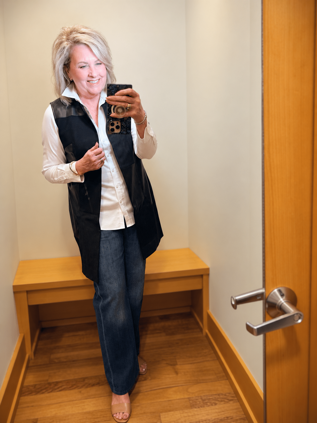 Woman over 50 wearing a Chico’s long black vest over a white shirt with dark-wash wide-leg jeans.