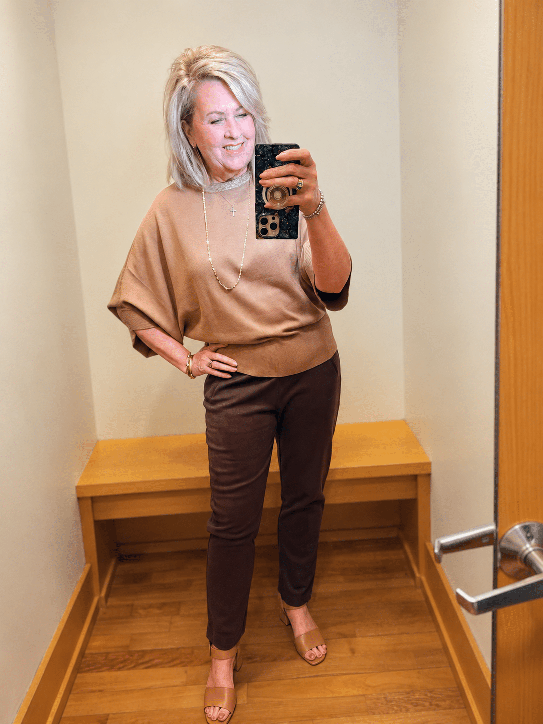 Woman over 50 wearing a Chico’s camel sequined cape sleeve sweater with chocolate brown slim ankle pants.