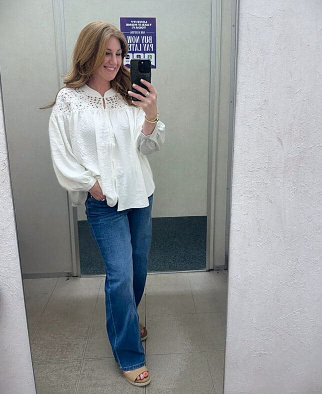 Petite woman wearing Cato's white long sleeve blouse and dark wash jeans